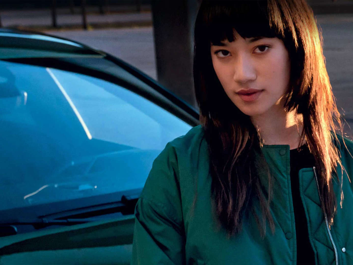 Дівчина в зеленій куртці стоїть перед автомобілем Peugeot